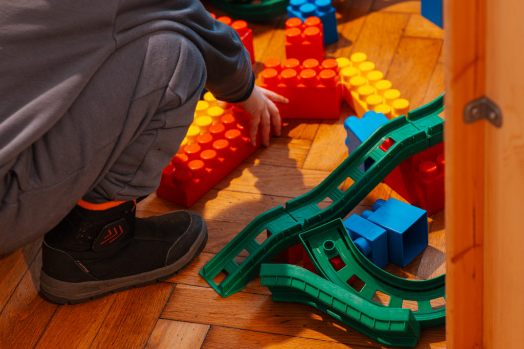 Na zdjęciu widać ręce dziecka wyciągnięte w stronę klocków do budowania ciuchci