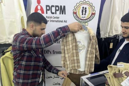 Na zdjęciu dwóch mężczyzn na tle roll-up'u PCPM, którzy wybierają ubrania dziecięce.