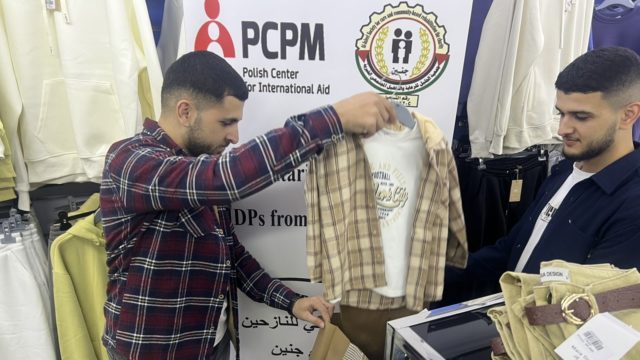 Na zdjęciu dwóch mężczyzn na tle roll-up'u PCPM, którzy wybierają ubrania dziecięce.