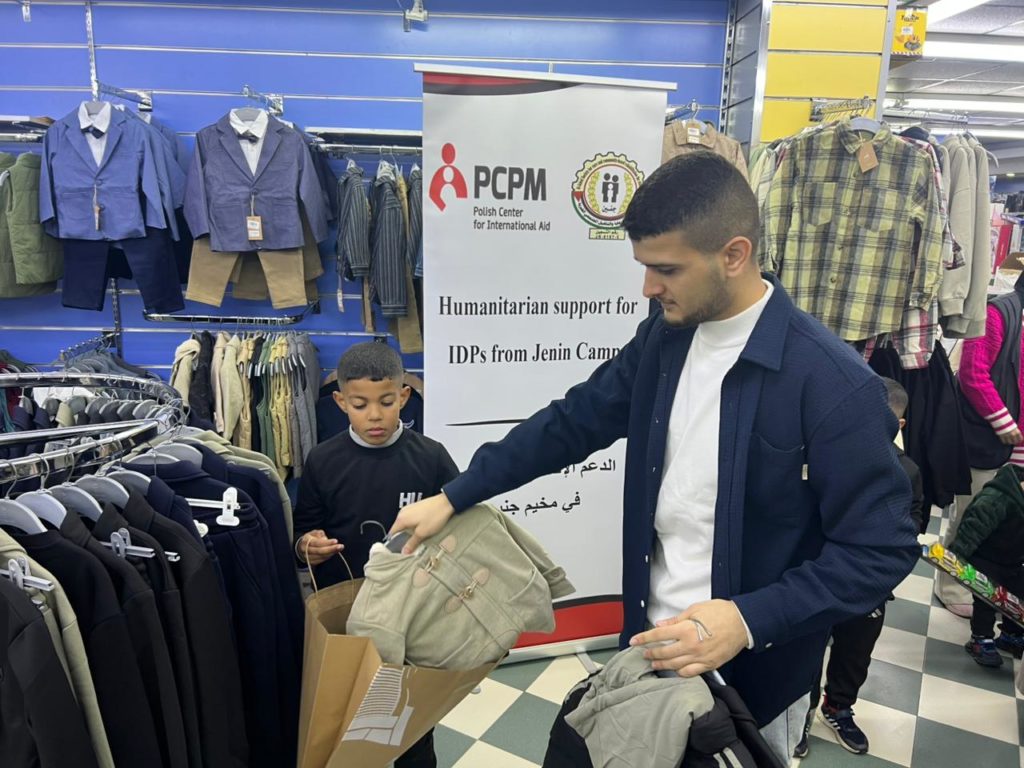 A boy and a man are together packing a bag with clothes for children 