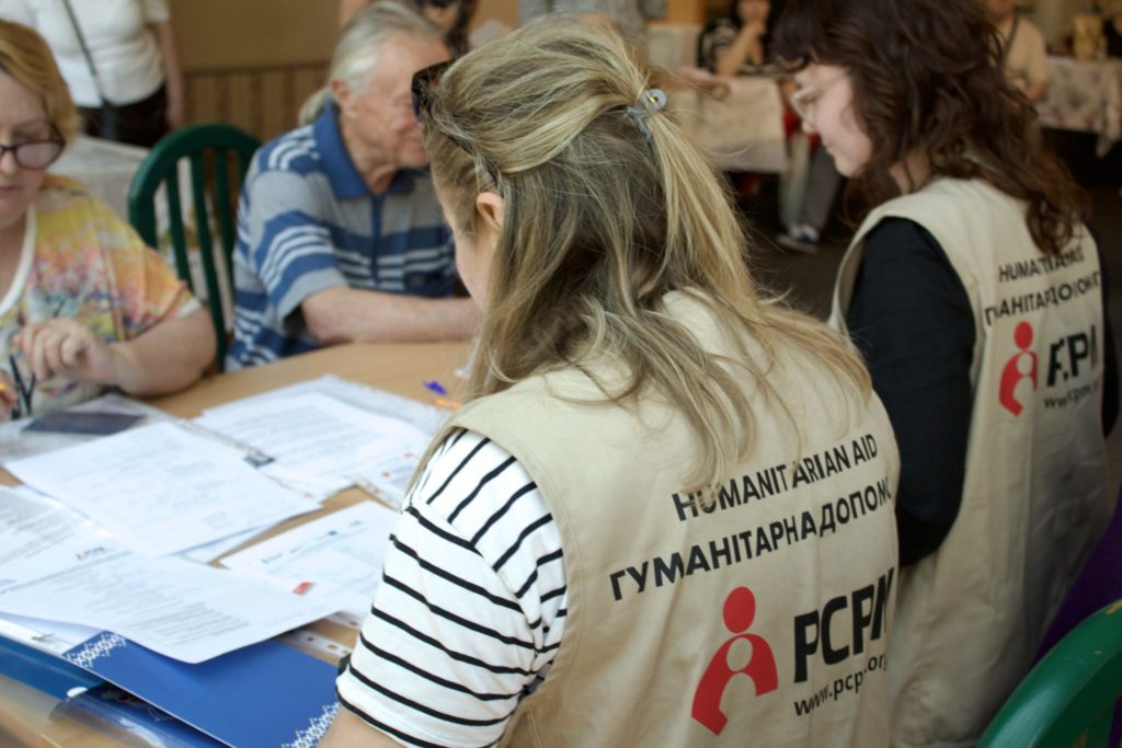 Na pierwszym planie widzimy w kamizelkach PCPM pracowniczki, które udzielają porad i pomagają uzupełniać dokumenty