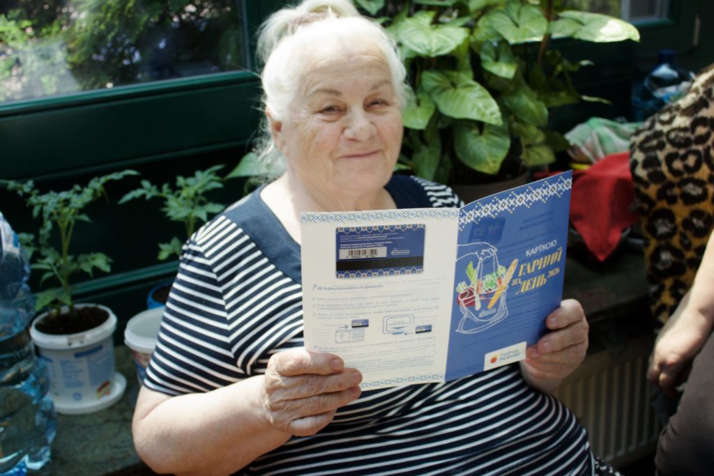Starsza kobieta siedzi i trzyma ulotkę informacyjną z wklejoną do środka wydaną jej kartą